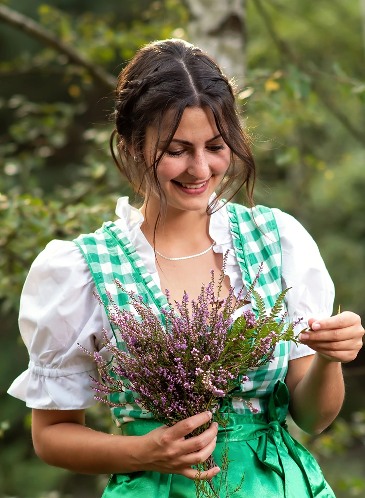 verspielte dirndl frisur mit geflochtenem detail und blumenstrauß
