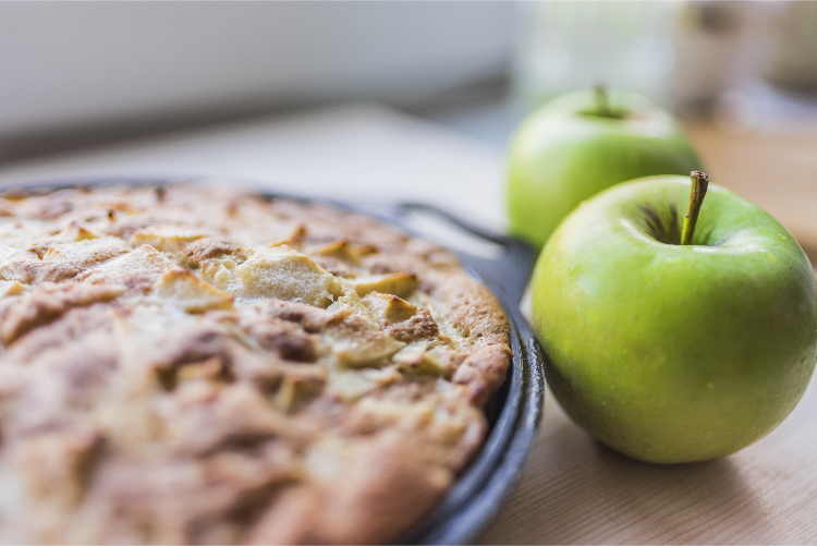 frisch gebackener apfelkuchen auf einem schwarzen backblech und zwei frische grüne Äpfel