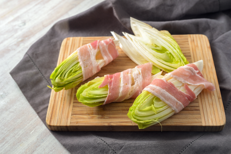 halbierte zichorien in streifen mit speck verpackt