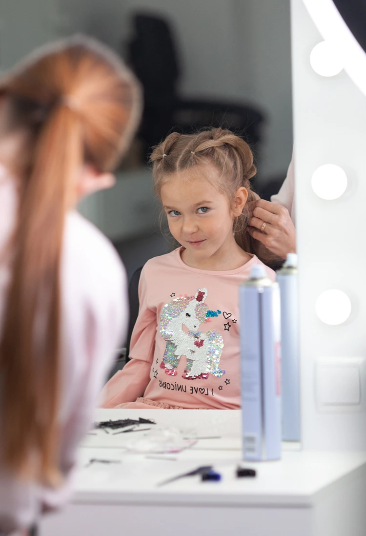 mädchen mit zwei zöpfe frisur schaut lächelnd in den spiegel im friseursalon