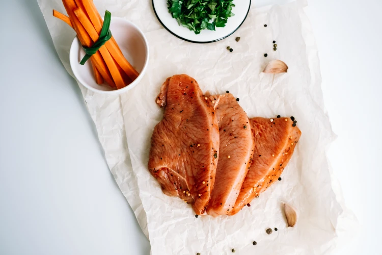mariniertes putensteak mit gewürzen auf einem backblech mit karottenstiften und kräutern