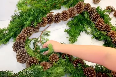 Mit Blumendraht Tannenzweige oder anderes Grün um die Zapfen binden