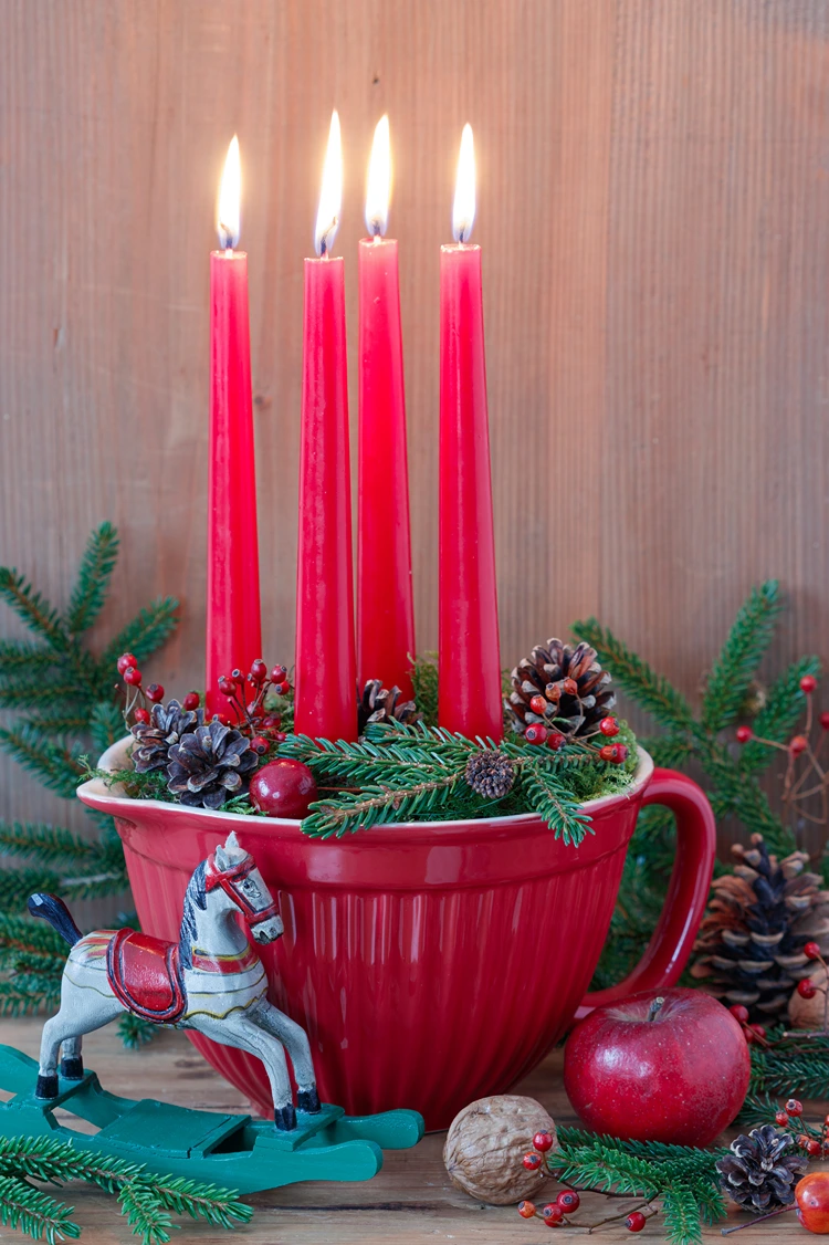 Rote Vintage-Kanne mit vier Tafelkerzen, gefüllt mit Tannenzapfen und Tannenzweigen